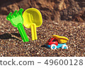 Children's toy truck with gravel or sand. Yellow scoop and green rake on the background. Concept of 49600128