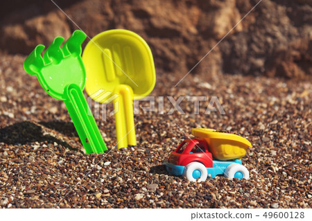 Children's toy truck with gravel or sand. Yellow scoop and green rake on the background. Concept of Children's toy truck with gravel or sand. Yellow scoop and green rake on the background. Concept of 49600128