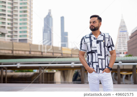 Young bearded Indian man thinking against view of sky train station Young bearded Indian man thinking against view of sky train station 49602575