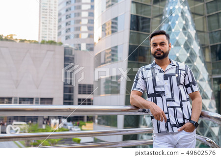 Young bearded Indian man taking selfie on footbridge in the city Young bearded Indian man taking selfie on footbridge in the city 49602576