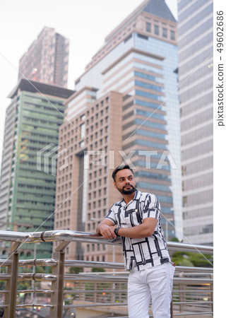 Young bearded Indian man thinking against view of the city Young bearded Indian man thinking against view of the city 49602686