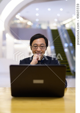Happy Asian businessman thinking while using laptop inside the office building 49605559