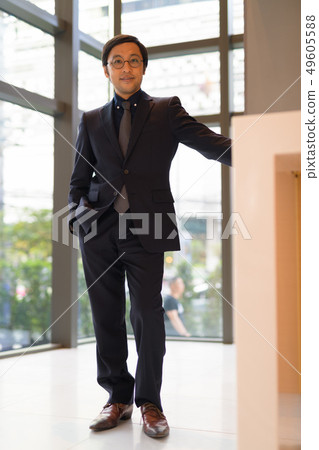 Full body shot of Asian businessman at the office by the window Full body shot of Asian businessman at the office by the window 49605588