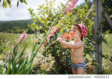 A small boy with a hat standing outdoors in garden in summer. 49609211
