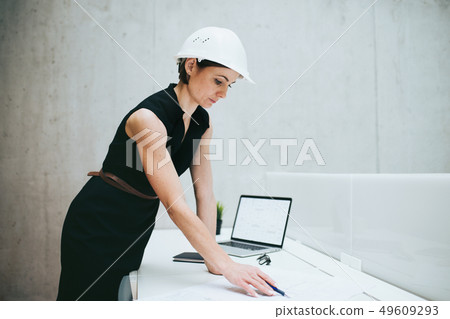 Young businesswoman or architect with helmet and laptop standing in office. 49609293