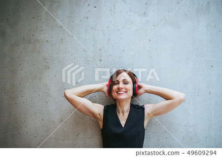 Young business woman with headphones standing against concrete wall in office. Young business woman with headphones standing against concrete wall in office. 49609294
