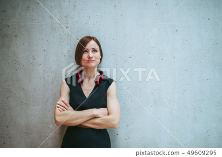 Young business woman with headphones standing against concrete wall in office. Young business woman with headphones standing against concrete wall in office. 49609295