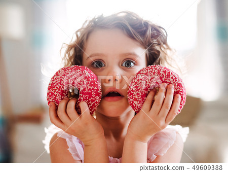 A small girl with doughnuts at home, looking at camera. A small girl with doughnuts at home, looking at camera. 49609388