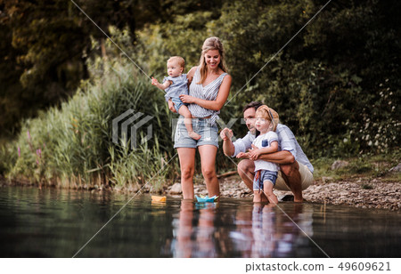 Young family with two toddler children outdoors by the river in summer, playing. 49609621