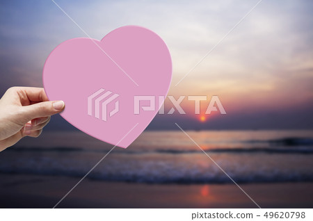 Woman hand holding pink paper heart on the beach 49620798