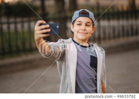 Young boy make a selfie on smartphone in the centre of the city. Cute boy in blue hat. Stylish Young boy make a selfie on smartphone in the centre of the city. Cute boy in blue hat. Stylish 49633792