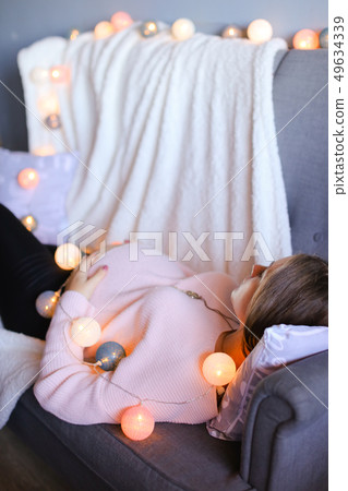 Pregnant caucasian woman lying on sofa near garlands. Pregnant caucasian woman lying on sofa near garlands. 49634339