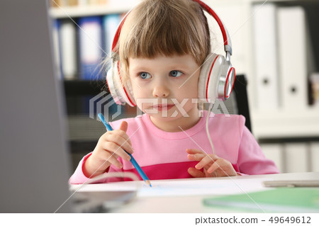 Little girl wearing headphones use mobile computer Little girl wearing headphones use mobile computer 49649612
