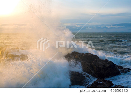 Waves of the Atlantic Ocean crashing against a rock at sunset. 49650380