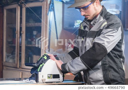 Portrait of a young carpenter joiner with manual circular power saw in the hands of a worker in a Portrait of a young carpenter joiner with manual circular power saw in the hands of a worker in a 49668790