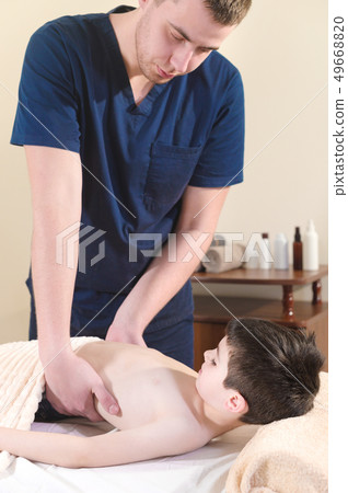 A male physiotherapist masseur makes a healing relaxing massage to a little smiling boy lying on a A male physiotherapist masseur makes a healing relaxing massage to a little smiling boy lying on a 49668820
