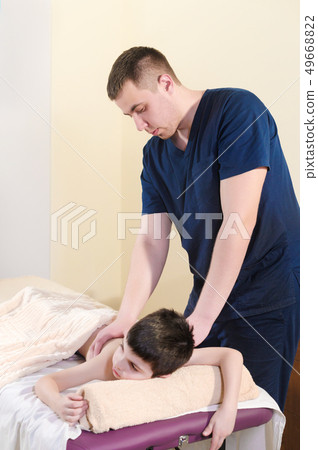 A little boy relaxes from a therapeutic massage. Male massage therapist makes a medical massage to A little boy relaxes from a therapeutic massage. Male massage therapist makes a medical massage to 49668822