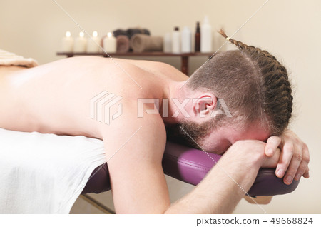 Male hipster with braided trendy hair and shaved temples lying on a massage bunk down face resting Male hipster with braided trendy hair and shaved temples lying on a massage bunk down face resting 49668824