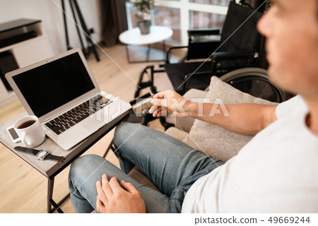 Disabled Man Sits on Sofa, Does Online Shopping Disabled Man Sits on Sofa, Does Online Shopping 49669244