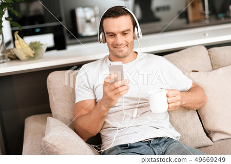 Man Listens to Music in Earphones and Drinks Tea Man Listens to Music in Earphones and Drinks Tea 49669249