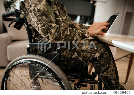 Military Man in Wheelchair Work on Laptop Indoors Military Man in Wheelchair Work on Laptop Indoors 49669405