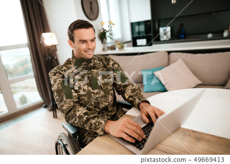 Military Man in Wheelchair Work on Laptop Indoors Military Man in Wheelchair Work on Laptop Indoors 49669413
