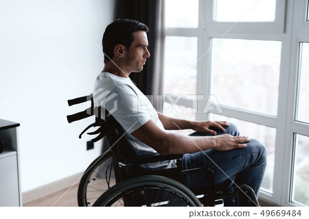 Disabled Person Sits in Wheelchair Against Window Disabled Person Sits in Wheelchair Against Window 49669484