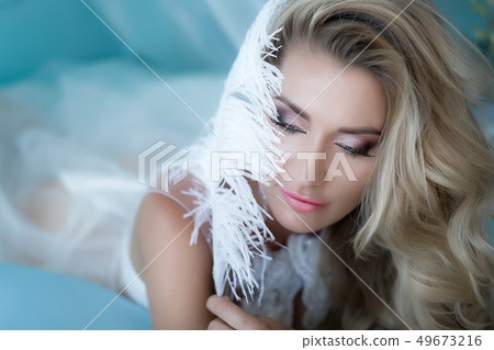 Boudoir photography. Woman blonde with long hair in lingerie on the bed surrounded by flowers tulips 49673216