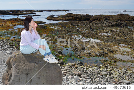 Shot portrait of a woman with dark hair perched on a rock on the beach of Mayor Isotana, Setana, Hokkaido Shot portrait of a woman with dark hair perched on a rock on the beach of Mayor Isotana, Setana, Hokkaido 49673616