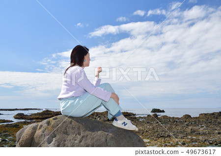 Shot portrait of a woman with dark hair perched on a rock on the beach of Mayor Isotana, Setana, Hokkaido Shot portrait of a woman with dark hair perched on a rock on the beach of Mayor Isotana, Setana, Hokkaido 49673617