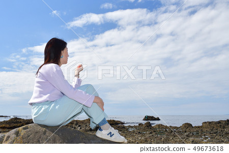 Shot portrait of a woman with dark hair perched on a rock on the beach of Mayor Isotana, Setana, Hokkaido Shot portrait of a woman with dark hair perched on a rock on the beach of Mayor Isotana, Setana, Hokkaido 49673618