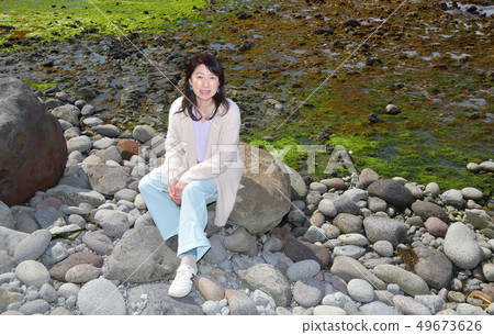 Shot portrait of a woman with dark hair perched on a rock on the beach of Mayor Isotana, Setana, Hokkaido 49673626