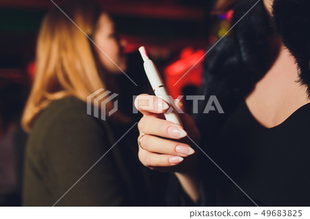 Electronic cigarettes, technology cigarette. Tobacco system IQOS. female hand on blurred background Electronic cigarettes, technology cigarette. Tobacco system IQOS. female hand on blurred background 49683825