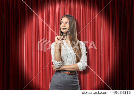 Young businesswoman thinking and looking away, holding glasses near lips, standing in spotlight near 49684316