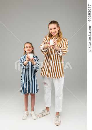 Pleasant smiling ladies in bright striped shirts showing glasses in their hands Pleasant smiling ladies in bright striped shirts showing glasses in their hands 49693027