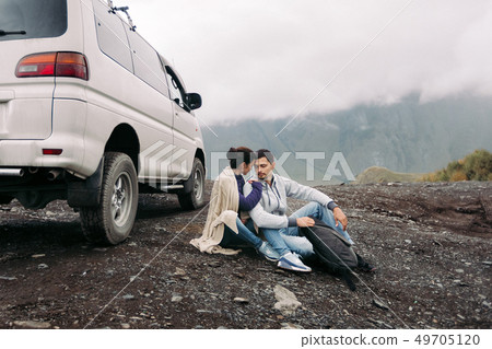 Loving couple sitting on a blanket near a car on a hillside 49705120