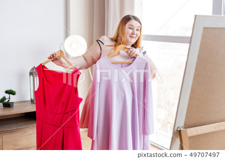 Joyful positive woman comparing two different dresses Joyful positive woman comparing two different dresses 49707497