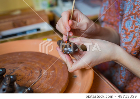 Professional woman potter painting ceramic souvenir penny whistle in pottery 49715359