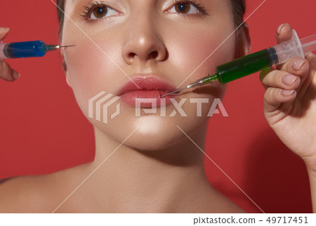 Face of young woman with two syringes near it Face of young woman with two syringes near it 49717451