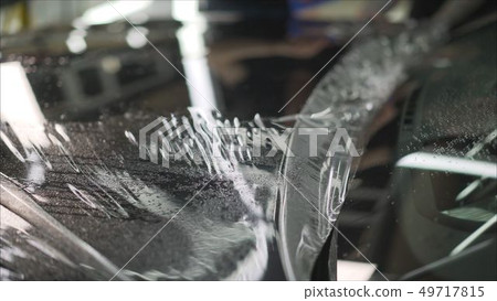 professional applying protective film to the red car. Master glues a protective film on the hood of professional applying protective film to the red car. Master glues a protective film on the hood of 49717815