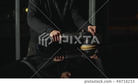 Car detailing - Hands with orbital polisher in auto repair shop. Polished black car. Car detailing - Hands with orbital polisher in auto repair shop. Polished black car. 49718233