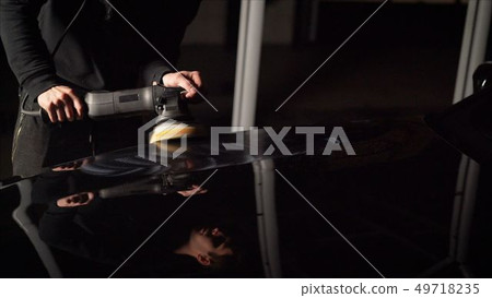 Car detailing - Hands with orbital polisher in auto repair shop. Polished black car. Car detailing - Hands with orbital polisher in auto repair shop. Polished black car. 49718235