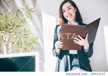 Woman checking file leaning on pillar at office Woman checking file leaning on pillar at office 49723737