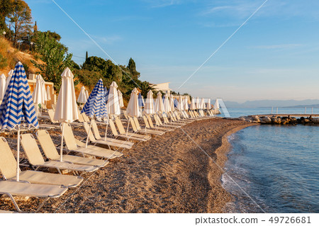 Summer sunrise on coast, Corfu island, Greece. Beach with Sunbeds and umbrellas with perfect views Summer sunrise on coast, Corfu island, Greece. Beach with Sunbeds and umbrellas with perfect views 49726681
