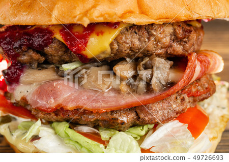 A big burger with two beef cutlets, cooked on charcoal. Lunch on a wooden background. The concept of A big burger with two beef cutlets, cooked on charcoal. Lunch on a wooden background. The concept of 49726693