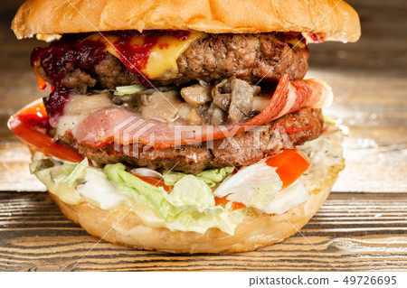 A big burger with two beef cutlets, cooked on charcoal. Lunch on a wooden background. The concept of A big burger with two beef cutlets, cooked on charcoal. Lunch on a wooden background. The concept of 49726695