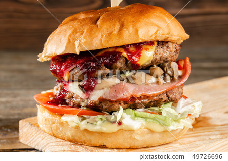 A big burger with two beef cutlets, cooked on charcoal. Lunch on a wooden background. The concept of A big burger with two beef cutlets, cooked on charcoal. Lunch on a wooden background. The concept of 49726696