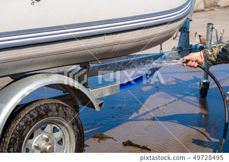 A man washes a rubber hose boat after going to sea. Drops of water scatter from the boat. A man washes a rubber hose boat after going to sea. Drops of water scatter from the boat. 49728495
