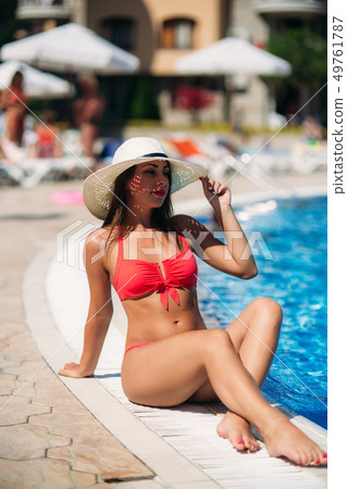 A Sexy lady in a big beach hat sunbathing by the the swimming pool. Beautiful model in pink swimsuit A Sexy lady in a big beach hat sunbathing by the the swimming pool. Beautiful model in pink swimsuit 49761787
