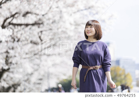 Woman taking a walk in a row of cherry blossom trees Woman taking a walk in a row of cherry blossom trees 49764255